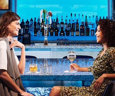 Two women have a conversation and drinks in the Delta Sky Lounge